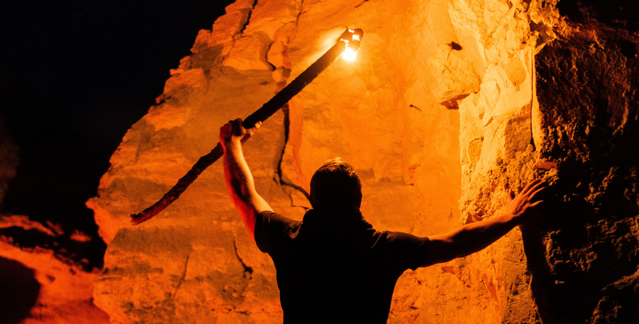 A man exploring a cave with a lit torch.